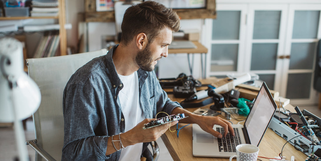 A man working at a cluttered desk with various electronic components, using a laptop to ensure adherence to EPR regulations in electronics recycling and design.